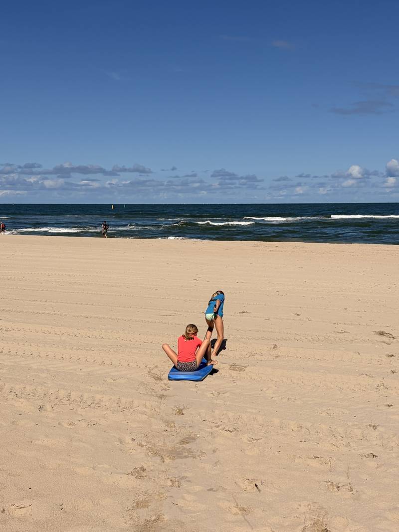 Two of my kids on a wide beach, one sitting on a bodyboard while the other pulls it across the sand.