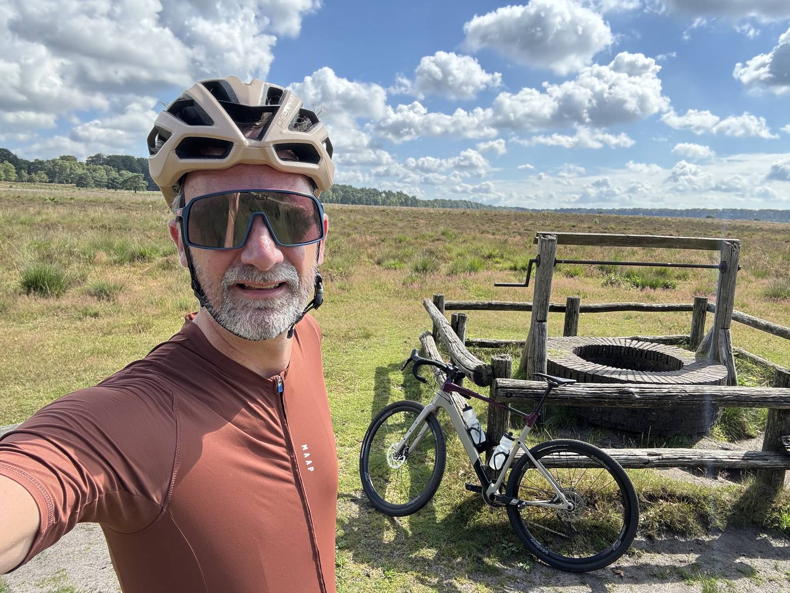 Me in cycling kit and a helmet, taking a selfie on open heathland with my gravel bike behind me.